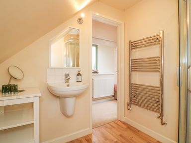 A bathroom with a wall-mounted sink mirror towel radiator and a small shelf unit at The Apple Barn at Wyke Farm in Lyme Regis