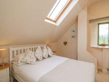 A bedroom with a double bed with floral pillows under a skylight window and a small window at The Apple Barn at Wyke Farm Lyme Regis
