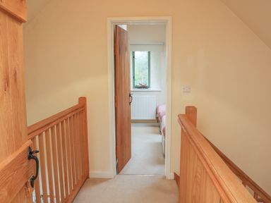 A hallway with wooden railing and an open wooden door leading to a room with a window and twin beds at The Apple Barn at Wyke Farm in Lyme Regis