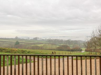 A view of a gravel pathway and green fields with trees and hedges behind a wooden fence at The Apple Barn at Wyke Farm in Lyme Regis