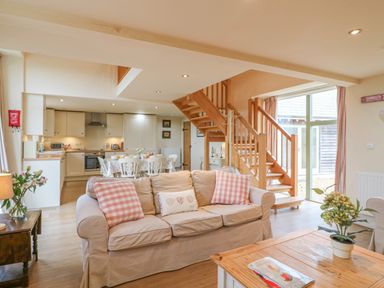 An open plan living room with beige sofa and wooden coffee table beside stairs at The Apple Barn at Wyke Farm in Lyme Regis