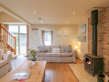 A living room with sofas a wooden coffee table plant a wood burning stove and stairs at The Apple Barn at Wyke Farm in Lyme Regis