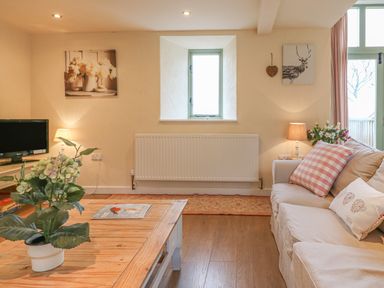 A living room with a beige sofa and pillows a wooden coffee table with a plant a small window and framed pictures at The Apple Barn at Wyke Farm in Lyme Regis