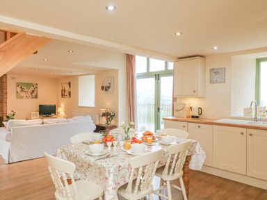 A kitchen and dining area with a table set for breakfast and a living room with a white sofa at The Apple Barn at Wyke Farm in Lyme Regis