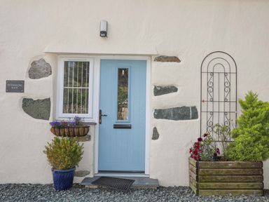 A blue door with a window and plants in pots outside at Ffynnon Bach in Deiniolen