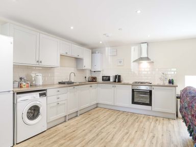 A kitchen with white cabinets a washing machine an oven a stove a microwave and a toaster at Ffynnon Bach in Deiniolen