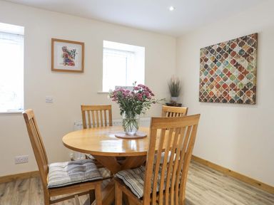 A dining room with a round wooden table and four chairs with cushions a vase with flowers on the table and decorative wall art at Ffynnon Bach in Deiniolen