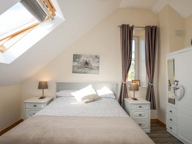 A bedroom with a bed between two nightstands with lamps and a wardrobe near a window at Ffynnon Bach in Deiniolen