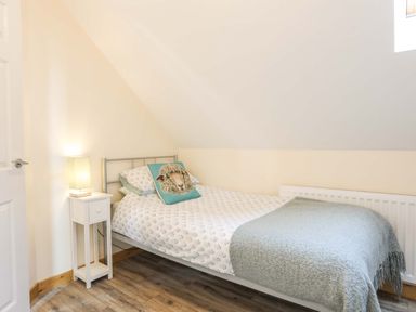 A bedroom with a single bed white bedside table with lamp and a sheep pillow at Ffynnon Bach in Deiniolen