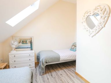 A bedroom with two single beds a white chest of drawers and a heart shaped mirror on the wall at Ffynnon Bach in Deiniolen