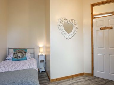 A bedroom with a single bed with sheep pillow bedside table and lamp and a heart shaped mirror on the wall at Ffynnon Bach in Deiniolen