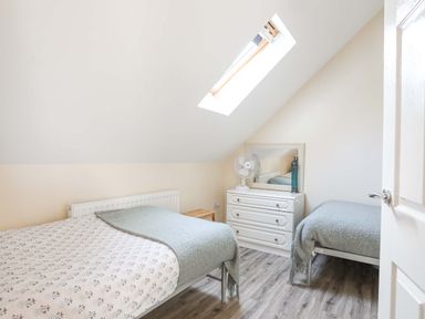 A bedroom with two single beds a chest of drawers a mirror and a skylight window at Ffynnon Bach in Deiniolen