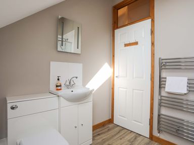 A bathroom with a white sink cabinet mirror white door and towel rail at Ffynnon Bach in Deiniolen