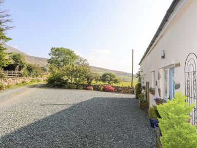 A gravel driveway next to a white building with potted plants and flowers at Ffynnon Bach in Deiniolen