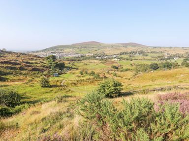 A rural landscape with grassy fields trees hills and a village in the distance at Ffynnon Bach in Deiniolen