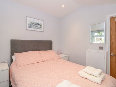 A bedroom with a bed with pink bedding two white nightstands a mirror on the wall and a wooden door at 201 Norton Park in Dartmouth