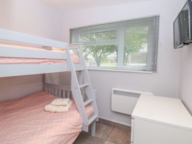 A bedroom with bunk beds with pink bedding a small white desk a wall-mounted TV and a window with blinds at 201 Norton Park in Dartmouth