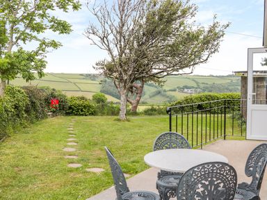 A patio with round metal table and chairs overlooking a garden with trees and a grassy field at 201 Norton Park in Dartmouth