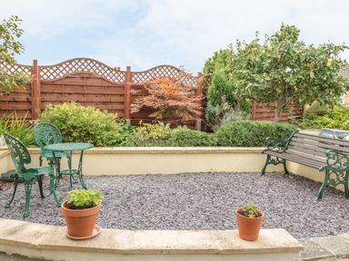 A small garden area with a wooden bench green metal table and chairs potted plants and a variety of shrubs and trees at Church Road Annexe in Cinderford
