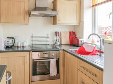 A kitchen with wooden cabinets an oven stovetop a sink with a red washing basin and kitchen utensils on countertops at Church Road Annexe in Cinderford