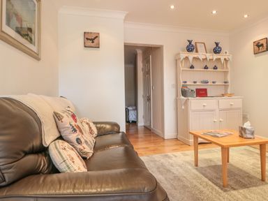 A living room with a leather sofa pillows and a wooden coffee table in front of a white cabinet with blue ceramics at Church Road Annexe in Cinderford