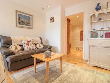 A living room with a leather sofa cushions a wooden coffee table a white cabinet and a painting on the wall at Church Road Annexe in Cinderford