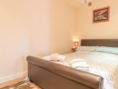 A bedroom with a bed covered in floral bedding two rolled towels on the bed a table lamp on a wall-mounted shelf and a framed picture on the wall at Church Road Annexe in Cinderford
