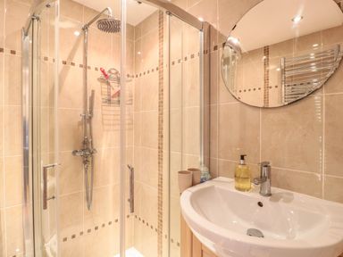 A bathroom with a glass shower enclosure and a sink with a round mirror above at Church Road Annexe in Cinderford