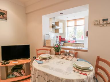 A dining area with a round table set for two near a kitchen with wooden cabinets and appliances at Church Road Annexe in Cinderford