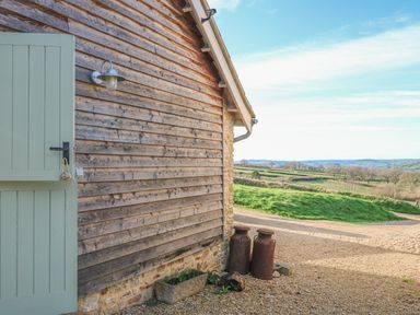 A wooden barn wall with a green door two metal milk cans and a view of grassy fields at The Shippon at Wyke Farm in Lyme Regis
