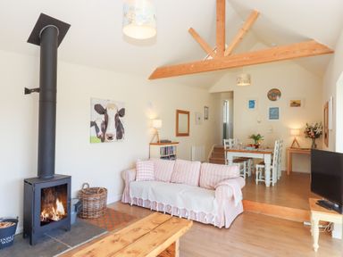 A living room with a wood stove next to a striped sofa and a dining table with white chairs at The Shippon at Wyke Farm in Lyme Regis