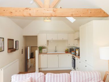 A kitchen with white cabinets and a sink with a striped sofa in front at The Shippon at Wyke Farm in Lyme Regis