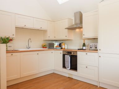 A kitchen with white cabinets a stainless steel oven stove and range hood a toaster a microwave and a bottle of champagne at The Shippon at Wyke Farm Lyme Regis