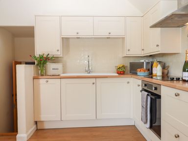 A kitchen with cream cabinets a sink stove oven a bowl of croissants and a vase of flowers at The Shippon at Wyke Farm Lyme Regis