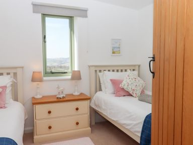 A bedroom with two single beds a window and a bedside table with lamps at The Shippon at Wyke Farm Lyme Regis