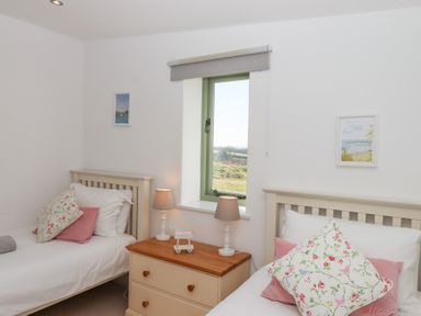 A bedroom with two single beds a window and a wooden bedside table with lamps at The Shippon at Wyke Farm in Lyme Regis
