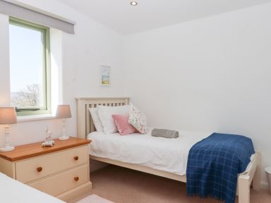 A bedroom with a single bed a bedside table with two lamps and a window at The Shippon at Wyke Farm in Lyme Regis