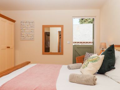 A bedroom with a bed pillows a pink throw a wardrobe a mirror and a half door at The Shippon at Wyke Farm Lyme Regis