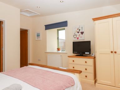 A bedroom with a bed a wooden chest of drawers with a television a wardrobe and a window at The Shippon at Wyke Farm in Lyme Regis