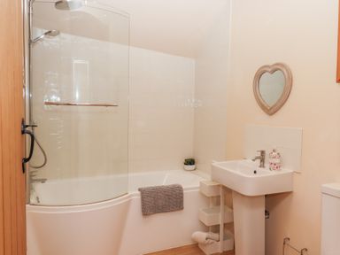 A bathroom with a bathtub and shower next to a sink under a heart shaped mirror at The Shippon at Wyke Farm in Lyme Regis