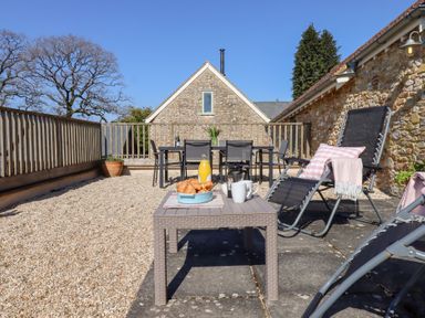 An outdoor patio area with lounge chairs a small table with breakfast items and a dining table with chairs at The Shippon at Wyke Farm in Lyme Regis