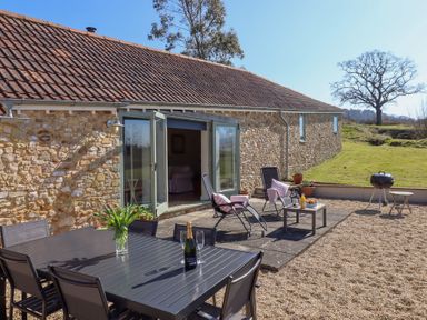A patio with a dining table and chairs a small table with drinks and chairs outside a stone building at The Shippon at Wyke Farm Lyme Regis