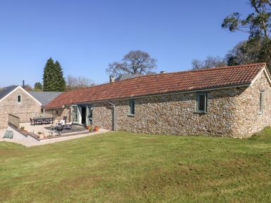 Stone building with tiled roof and outdoor seating area on a grassy slope at The Shippon at Wyke Farm in Lyme Regis