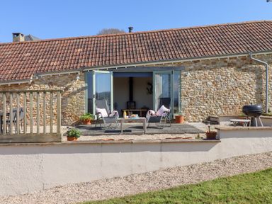 A stone building with an outdoor patio featuring two chairs a table with drinks and snacks and a barbecue grill at The Shippon at Wyke Farm Lyme Regis