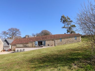 A stone building with a tiled roof on a grassy slope with trees around at The Shippon at Wyke Farm in Lyme Regis