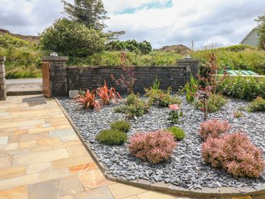 A garden bed with various plants and shrubs surrounded by slate stones next to a paved area and stone wall at Sea View Hideaway in Lahinch County Clare