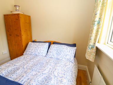 A bedroom with a double bed with patterned bedding next to a wooden wardrobe and a window with floral curtains at Sea View Hideaway in Lahinch County Clare