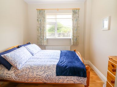 A bedroom with a bed a window with curtains and a wooden dresser at Sea View Hideaway in Lahinch County Clare