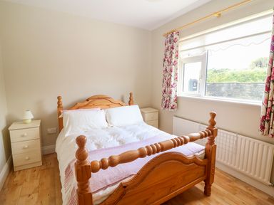 A bedroom with a wooden bed white bedding two bedside tables a window with floral curtains and a radiator at Sea View Hideaway in Lahinch County Clare
