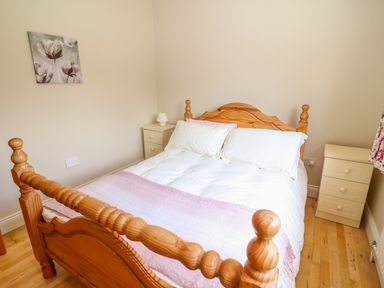 A bedroom with a wooden bed frame white bedding two bedside tables with lamps and a floral painting on the wall at Sea View Hideaway in Lahinch County Clare